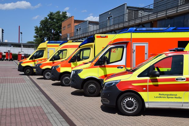 Das Bild zeigt vier Rettungswägen und einen Notarztwagen auf einem Parkplatz.