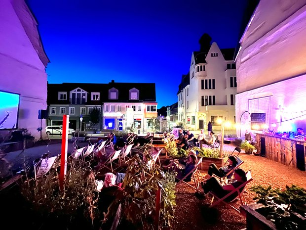 Das Bild zeigt ein Outdoorkino mit Liegstühlen am Abend