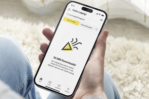 Eine Hand hält ein Smartphone, auf dem die Leipzig App geöffent ist: "50.000 Downloads!"