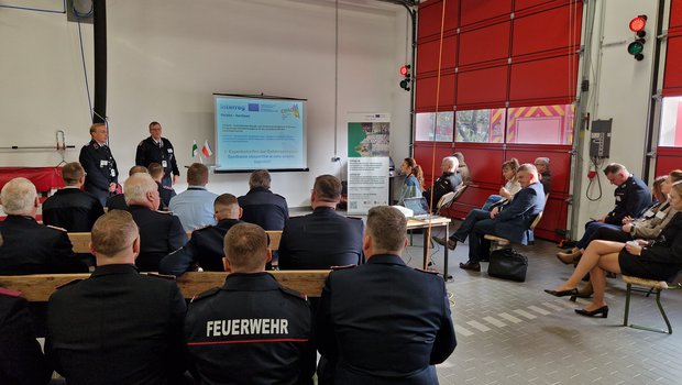 Mehrere Personen sitzen in einem Raum der Feuerwerhr und das Projekt wird präsentiert.