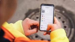 Hände halten ein Smartphone mit der laufenden App vor einem Straßenablauf