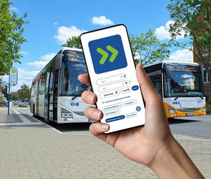 Ein Hand hält ein Smartphone mit der App vor einer Haltstelle.